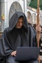Portrait of a pensive elderly monk 45-50 years old in a black cassock sitting at a laptop against the background of the city. Conc