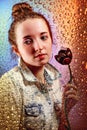 Portrait of pensive girl with black tulip behind window glass with drops of rain and colorful reflection from rainbow or Royalty Free Stock Photo