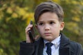 Portrait of pensive little businessman talking by phone on autumn background. The development of modern children concept Royalty Free Stock Photo