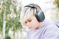 Portrait of pensive lonely teenager boy sitting on the park and listening to music on wireless headphones Royalty Free Stock Photo