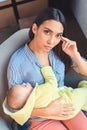 portrait of pensive mother with infant baby resting on arm chair