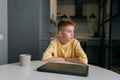 Portrait of pensive redhaired 10 year old boy sitting in front of closed laptop, thoughtful looking away. Front view of Royalty Free Stock Photo