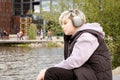 Portrait of pensive sad caucasian teenager boy sitting on the lake shore and listening to music on wireless headphones Royalty Free Stock Photo