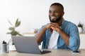 Portrait of pensive smiling black freelancer sitting at desk in home office