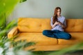 Portrait of pensive stressed young woman sitting on sofa at home using smartphone looking away pondering of problem Royalty Free Stock Photo