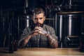 Portrait of a pensive tattooed hipster male with stylish beard and hair in the shirt in indie brewery.