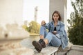 Portrait of a pensive teenage girl dressed in denim and boots, sitting, looking at camera. Horizontal view.