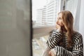 Portrait of pensive thoughtful blond pretty dreaming depressed woman sitting window sill looking distance street. Side Royalty Free Stock Photo