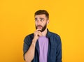 Portrait of pensive young bearded man touching his chin, deep in thought over orange studio background Royalty Free Stock Photo