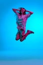 Portrait of pensive, young girl wearing casual clothes jumping in air with closed eyes over blue background in neon Royalty Free Stock Photo