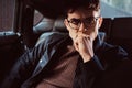 A pensive young man wearing glasses sitting in the back seat of the car. Royalty Free Stock Photo