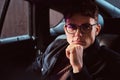 A pensive young man wearing glasses sitting in the back seat of the car. Royalty Free Stock Photo