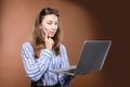 Portrait of a pensive young woman with long hair in a shirt holds her laptop in her hands and thinks puzzled. Question Royalty Free Stock Photo