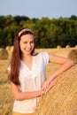 Portrait of a perky smiling girl standing against a background of bales of straw. Closeup. Vertical