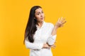 Portrait of perplexed bewildered young woman in white casual shirt looking camera, spreading hand isolated on yellow