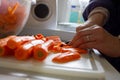 A portrait of a person chopping up carrots into small pieces on a cutting board in a kitchen with a sharp knife. The orange Royalty Free Stock Photo