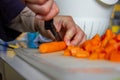 A portrait of a person chopping up carrots into small pieces on a cutting board in a kitchen with a sharp knife. The orange Royalty Free Stock Photo