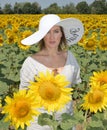Portrait pf a young and beautiful woman looking at the camera in a sunflower field wearing an oversized hat Royalty Free Stock Photo