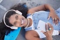 Portrait, phone and music with a black woman skater lying on her board at a skatepark from above. Face, skating and