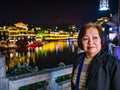 Portrait photo of Asian senior woman with beautiful nightscape of fenghuang old town.