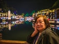 Portrait photo of Asian senior woman with beautiful nightscape of fenghuang old town.