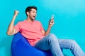 Portrait photo of overjoyed crazy young man raised fist up betting sports using smartphone sit pouf isolated on Royalty Free Stock Photo