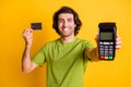 Portrait photo of smiling cheerful man keeping bank credit card smiling showing blurred terminal isolated on vivid