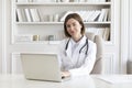 Portrait photo of young and beautiful smiling female doctor sitting and working on laptop in the office of the modern clinic Royalty Free Stock Photo