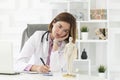 Portrait photo of young thinking female doctor in white medical gown sitting and working on laptop in the modern clinic Royalty Free Stock Photo