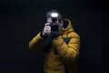 Photographer in a yellow coat taking a photo with flash with a black background