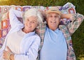 Portrait, picnic and an elderly couple lying on a blanket in a field together for romance or bonding from above. Relax