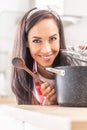 Portrait picture of a good looking girl smelling from a pot, opening a lid, holding a wooden spoon