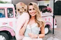 Portrait of pin up styled girl with long blonde hair on retro coffee car background. She holds pink fur stole on