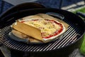 A portrait of a pizza margherita lying on a pizza stone and a piece of baking paper on a charcoal barbecue grill. The delicious Royalty Free Stock Photo