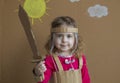 Clouse-up portrait of cheerful little girl with a cardboard sword and a suit. handmade. background of painted sun and