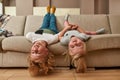 Portrait of playful kids, little boy and girl smiling while lying upside down on a sofa in the living room