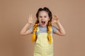 Portrait of playful little girl with yellow kanekalon pigtails, pretending to be scary frightening with hands and opened