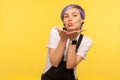 Portrait of playful lovely hipster girl holding her palms up and blowing kiss. yellow background, studio shot