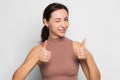 Portrait of playful and sweet young woman giving wink and showing thumbs up sign, giving recommendation or approval like. Standing Royalty Free Stock Photo