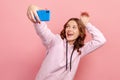 Portrait of playful teenage girl in hoodie gesturing bunny ears and smiling on smartphone camera, having fun, taking selfie