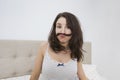 Portrait of playful woman with mustache made of hair in bed