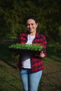 Portrait of a pleasant hardworking multiethnic woman farmer standing in a greenhouse, holding a cassette with seedlings in her Royalty Free Stock Photo