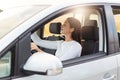 Portrait of pleasant looking female with dark hair being satisfied her journey driving car, sitting on driver`s seat, looking in