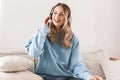 Portrait of pleased blond girl 20s wearing headphones smiling and listening to music at home Royalty Free Stock Photo