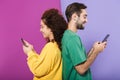 Portrait of pleased caucasian couple in colorful clothing smiling and holding cellphones standing back to back