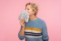 Portrait of pleased happy woman with curly hair in warm sweater smelling dollar banknotes and closing eyes