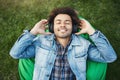 Portrait of pleased and happy young african-american lying on bean bag chair while being in park, enjoying listening Royalty Free Stock Photo