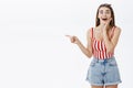 Portrait of pleased and interested good-looking european woman in striped top and shorts pointing intrigued left