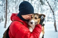 Portrait pleased man embracing dog Welsh Corgi with eyes closed outdoors in winter landscape