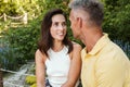 Portrait of pleased middle-aged couple smiling at each other while sitting in summer park